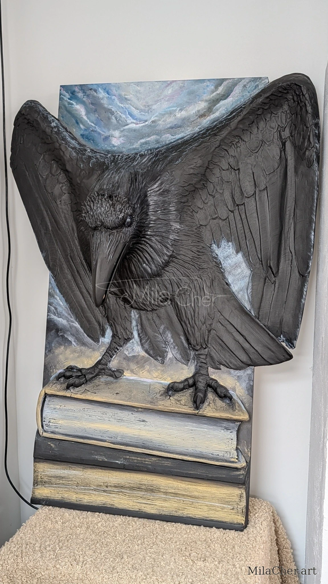 Finished black sculptural raven with outstretched wings standing on books